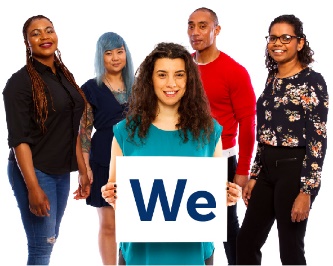 A woman standing in front of a group of people. She is holding up a sign that says 'We'.
